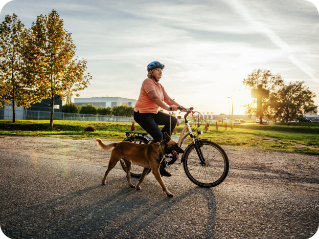 Woman riding her bike at sunset while her dog walks beside her