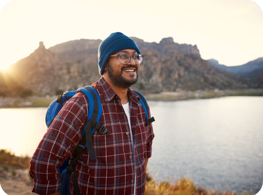 Man in a winter hat walking beside a lake and the mountains smiling