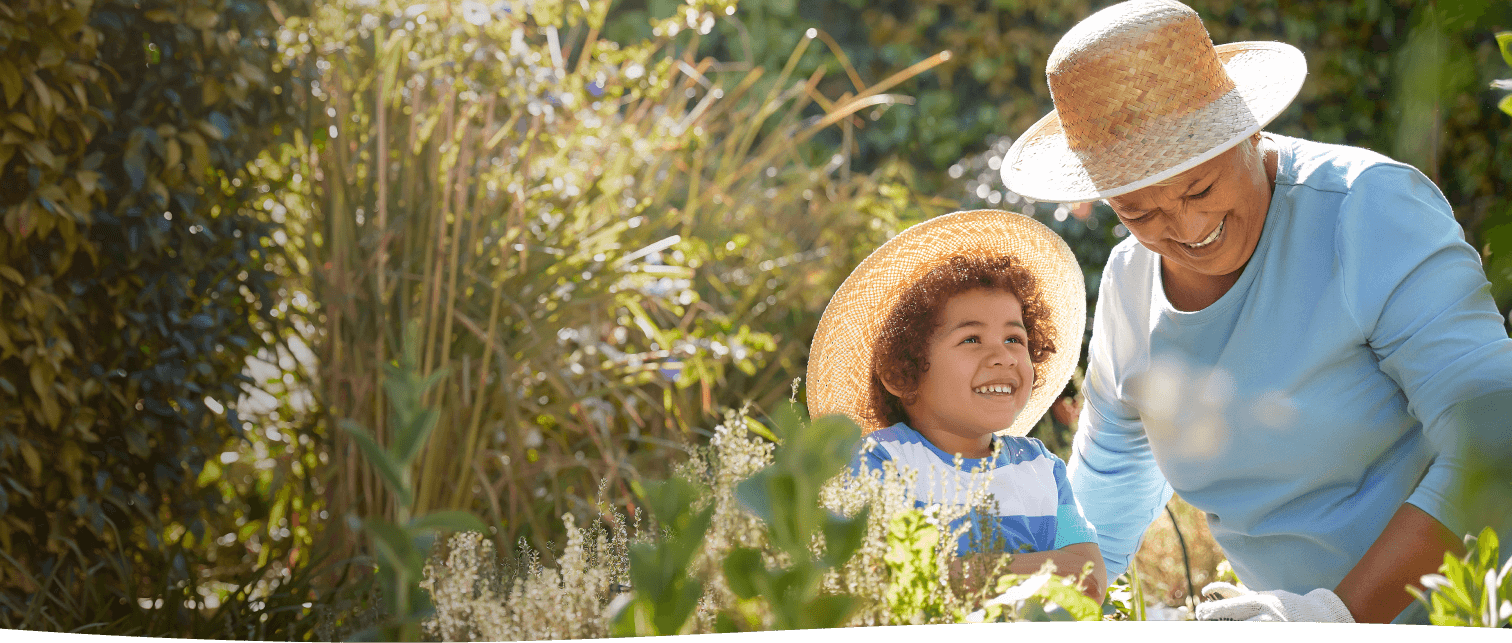 Grandmother and grandchild smiling while gardening together in sun hats